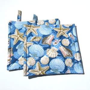 May include: Two blue pot holders with a seashell and starfish pattern. The pot holders are quilted and have a loop for hanging.