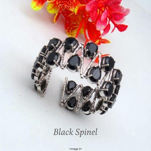 May include: A silver cuff bracelet featuring a zigzag wire design set with multiple pear-shaped black spinel gemstones. The open-ended bracelet displays a repeating geometric pattern of polished metal and dark stones, labelled Black Spinel.