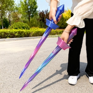 May include: Two toy swords with a gradient design. One sword has a blue handle and guard, transitioning to purple and pink on the blade. The other sword has a pink handle and guard, transitioning to blue and purple on the blade.