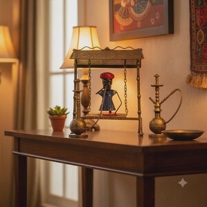 May include: A metal swing set featuring a figurine wearing a red turban and blue tunic, flanked by two brass-colored hookahs. The swing has a perforated roof and chain supports. A small potted succulent sits to the left of the central display.