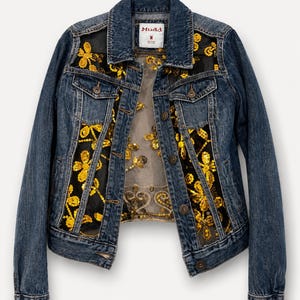 May include: A medium-wash blue denim jacket featuring sheer black mesh panels on the front. The mesh is decorated with bright yellow floral embroidery and gold sequins. The jacket has a standard collar, button-front closure, and a Mudd brand label.