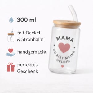 May include: A clear glass tumbler with a 300 ml capacity, featuring a bamboo lid and a glass straw. The glass is printed with a pink heart and the German text MAMA DU BIST MEINE HELDIN. The design includes icons for a lid, straw, handmade, and gift.