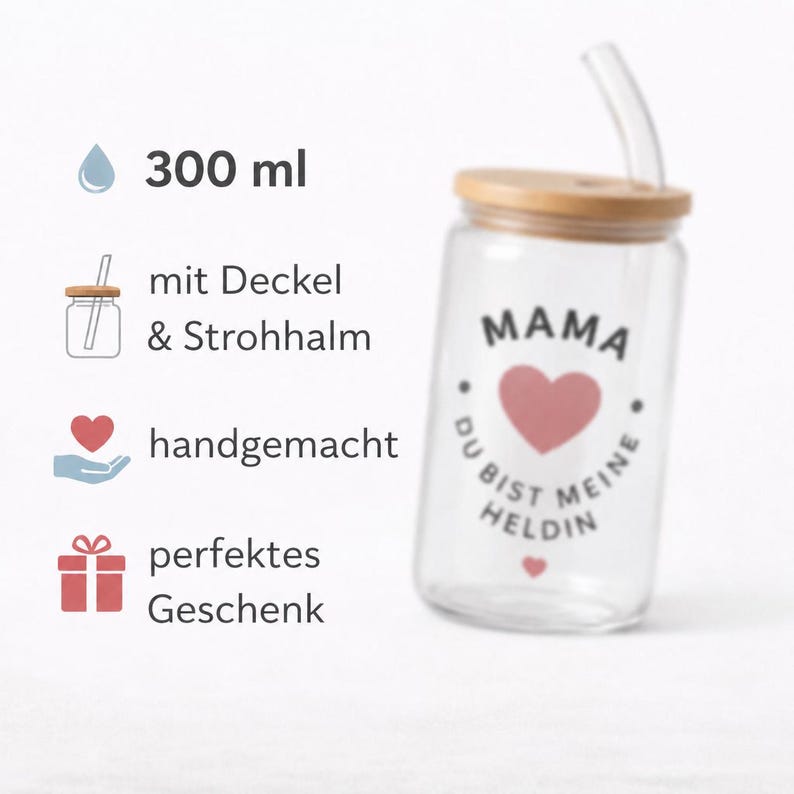 May include: A clear glass tumbler with a 300 ml capacity, featuring a bamboo lid and a glass straw. The glass is printed with a pink heart and the German text MAMA DU BIST MEINE HELDIN. The design includes icons for a lid, straw, handmade, and gift.