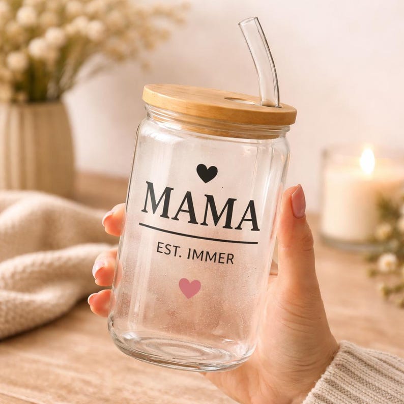 May include: A clear glass tumbler with a bamboo lid and a curved glass straw. The glass features the black text MAMA above a horizontal line, with the text EST. IMMER below it, accompanied by a small black heart above and a pink heart below.