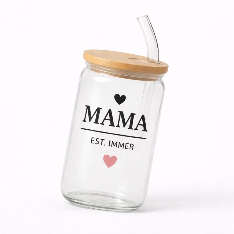 May include: A clear glass tumbler with a bamboo lid and a curved glass straw. The glass features the black text MAMA above a horizontal line, with EST. IMMER printed below. A small black heart is above the text and a pink heart is below.
