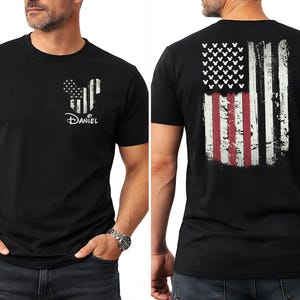 K&ouml;nnte beinhalten: Schwarzes T-Shirt mit einem verblassten amerikanischen Flaggen-Design auf dem R&uuml;cken und einer von Mickey Mouse inspirierten Flagge auf der Vorderseite. Das Frontdesign enth&auml;lt den Namen "Daniel". Das T-Shirt ist kurz&auml;rmelig.