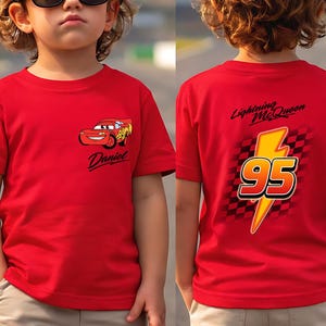 Pu&ograve; includere: Maglietta rossa con Saetta McQueen del film Cars. La parte anteriore mostra il personaggio e il nome "Daniel". Il retro presenta un fulmine giallo con il numero "95" e il testo "Lightning McQueen".