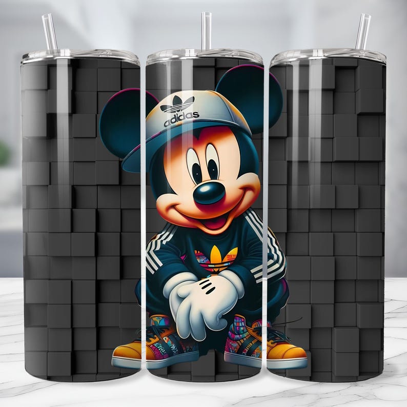 May include: A stainless steel tumbler featuring a cartoon illustration of Mickey Mouse in a black Adidas tracksuit and hat. The design includes white stripes, a colorful shoe design, and a black background with a 3D cube pattern. The tumbler has a clear straw.