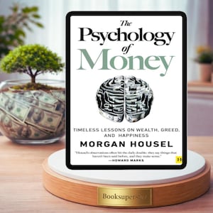Puede incluir: Una tableta digital muestra el libro "The Psychology of Money" de Morgan Housel. La portada presenta un laberinto con forma de cerebro. El libro está sobre un expositor. Un pequeño árbol en un cuenco de cristal lleno de dinero está al fondo.