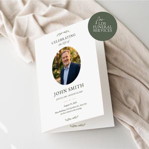 Puede incluir: Un programa funerario blanco plegado con una foto ovalada central de un hombre con blazer azul. El texto dice CELEBRATING the life of JOHN SMITH, JULY 25, 1965 - AUGUST 22, 2025, August 25, 2025, Main Building, 123 Anywhere St., Any City.