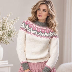 May include: A long-sleeved knit sweater featuring a cream-colored base with a decorative yoke pattern in shades of pink and grey. The sweater has a ribbed grey crew neckline, ribbed grey cuffs, and a ribbed grey hemline at the waist.
