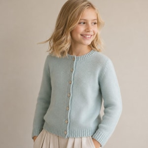 May include: A light blue long-sleeve knit cardigan featuring a round neckline and a vertical row of six small, round, light-colored buttons down the center front. The garment has ribbed cuffs and a ribbed hem, with a smooth, consistent knit texture.