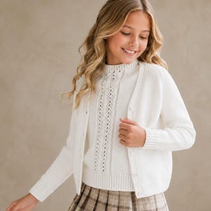 May include: A white long-sleeve knit cardigan with a button-down front and a matching white knit sweater underneath featuring a vertical eyelet lace pattern, paired with a brown and tan plaid pleated skirt with a classic checkered design.
