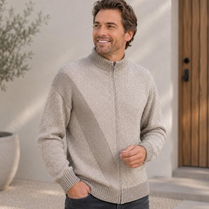 Könnte beinhalten: Ein beigefarbener Strickpullover mit durchgehendem Reißverschluss, Stehkragen, langen Ärmeln mit gerippten Bündchen und einem gerippten Saum. Das Kleidungsstück zeigt ein dezentes, diagonal verlaufendes Strukturmuster auf der Vorderseite.