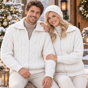 May include: Two matching white knit zip-up sweaters with a textured cable pattern, wide collars, and ribbed cuffs. Each sweater features a full-length silver zipper closure down the center, worn over a neutral-toned turtleneck base layer.