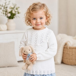 May include: A white long-sleeved knit jumper featuring vertical openwork patterns, a ribbed crew neckline, and small decorative bows on the front. The jumper is paired with a light blue skirt and held with a small beige plush rabbit toy.