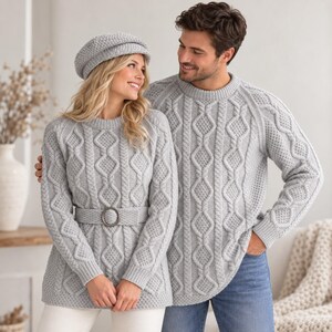 May include: A light grey cable knit jumper with a matching belt featuring a circular buckle, paired with a matching cable knit beret. Beside it, a light grey cable knit jumper with a crew neckline and long sleeves worn with blue jeans.