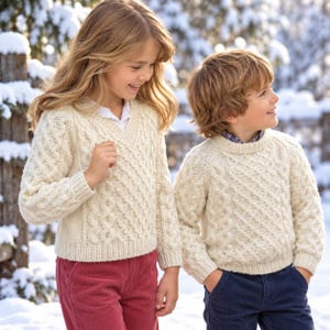 May include: Two cream-coloured cable knit jumpers featuring intricate textured patterns. One jumper has a V-neckline and long sleeves, while the other is a crew neck style with long sleeves. Both garments are crafted with a thick, warm knit construction.