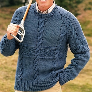 May include: A blue knit sweater with cable knit and textured panel details. The sweater has a crew neck and raglan sleeves. The sleeves and front panels feature intricate cable patterns. The sweater is a solid blue color.