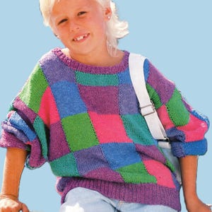 May include: A colorful, patchwork-style sweater in shades of pink, green, blue, and purple. The sweater has a ribbed collar, cuffs, and hem. The design features large, square blocks of color. The sleeves are three-quarter length.