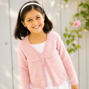 May include: A light pink knit cardigan featuring long sleeves, a ribbed collar, and a single button closure at the centre front. The garment is worn over a white top and has a textured knit pattern along the neckline and front edges.