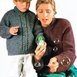 Puede incluir: Una mujer y un niño soplan burbujas. La mujer lleva un suéter marrón, el niño uno azul y verde. Los suéteres tienen un patrón de punto texturizado. Las burbujas flotan en el aire.