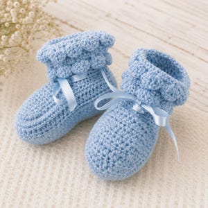 May include: A pair of light blue crochet baby booties featuring a textured bobble stitch cuff and a matching light blue satin ribbon tied in a bow at the front. The booties are constructed with a dense, uniform stitch pattern throughout the foot.