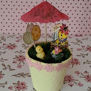 May include: A white ceramic mug with a black handle and the text "But First, Coffee" in a black, handwritten-style font. The mug is on a white surface.