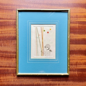 May include: Framed artwork featuring a whimsical illustration of a child with wings, holding colorful strings and balloons. The artwork is in a blue mat with a gold frame, creating a charming and artistic piece.