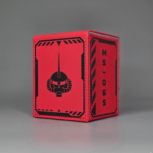 Red Gundam inspired trading card deck box shown at an angle with mobile suit head emblem and MS-06S text panel. Char's Zaku II