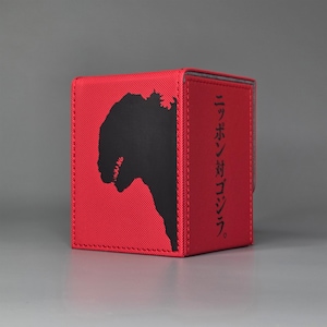 Op de afbeelding: Rode opbergdoos met een zwart silhouet van een monster aan één kant. Japanse tekst is zichtbaar op de zijkant. De rechthoekige doos is gemaakt van een getextureerd materiaal en heeft gestikte randen.