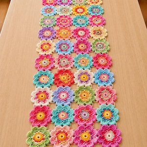 May include: A rectangular table runner made of interconnected crocheted flower motifs in a vibrant array of colors including pink, blue, yellow, green, and purple. Each individual flower features a central circular core with radiating petals.