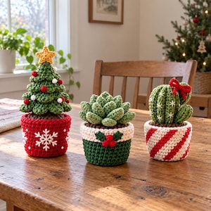 May include: Three crocheted plants in decorative pots. The left is a green Christmas tree with a yellow star, red and white pom-poms in a red pot with a white snowflake. The center is a green succulent in a green and cream pot with holly. The right is a green cactus with a red bow in a red and white striped pot.