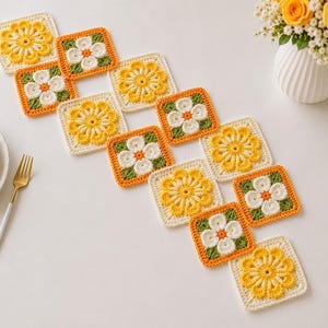 May include: A crochet table runner composed of interconnected square motifs featuring floral patterns in yellow, white, and green yarn. The runner is arranged in a diagonal, staggered formation across a white surface with plates and gold forks.