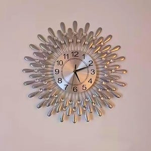 May include: Silver wall clock with a sunburst design. The clock face is silver with black numerals and hands. Clear crystals are set around the clock face and on the sunburst rays. A decorative piece for any room.