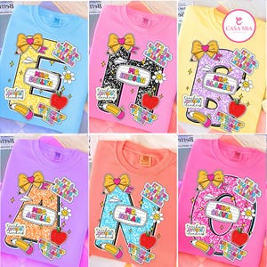 May include: Six crewneck sweatshirts in light blue, pink, yellow, purple, peach, and bright pink. Each features a large letter with a patterned fill, a name tag, a yellow bow, a red apple, a pencil, and text including It's a beautiful day for learning.
