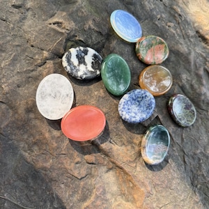 May include: A white ceramic mug with a black handle and the text "But First, Coffee" in a bold, black font. The mug is set against a blurred background, suggesting a cozy setting.