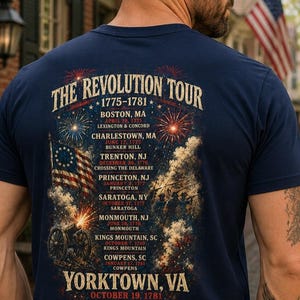 May include: A navy blue t-shirt featuring a graphic on the back titled The Revolution Tour 1775-1781. The design lists historical locations and dates including Boston, Charlestown, Trenton, Princeton, Saratoga, Monmouth, Kings Mountain, Cowpens, and Yorktown.