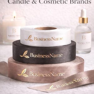 May include: Three stacked rolls of satin ribbon in white, dark brown, and light brown, each featuring a gold foil logo with a leaf icon and the text BusinessName. The text Custom Ribbon for Candle & Cosmetic Brands and Premium Packaging & Branding is visible.