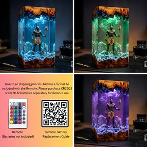 May include: A rectangular resin lamp featuring a miniature Anubis figure holding a staff, surrounded by stone-like structures. The lamp emits blue, green, or purple light, creating a smoky effect within the clear resin and wood base.