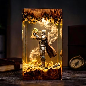 May include: A rectangular resin lamp featuring a miniature figure of a silver-armoured warrior holding a small green creature. The scene is encased in clear resin with a natural wood base and top, illuminated from within by a warm, glowing light.