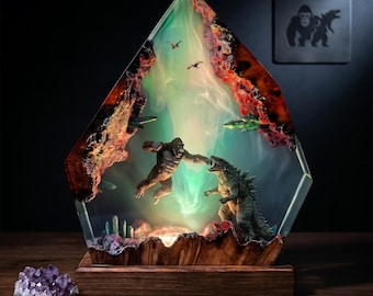 May include: A resin and wood lamp featuring a diorama of a gorilla and a lizard-like creature in a combat pose. The piece has a glowing green light effect, red and brown wood accents, and a small amethyst cluster sitting on the base nearby.