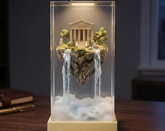 May include: A rectangular clear acrylic lamp featuring a miniature floating island with a classical Greek temple, green trees, and two cascading waterfalls. The base is light wood, and the top has a black light fixture emitting a warm glow.