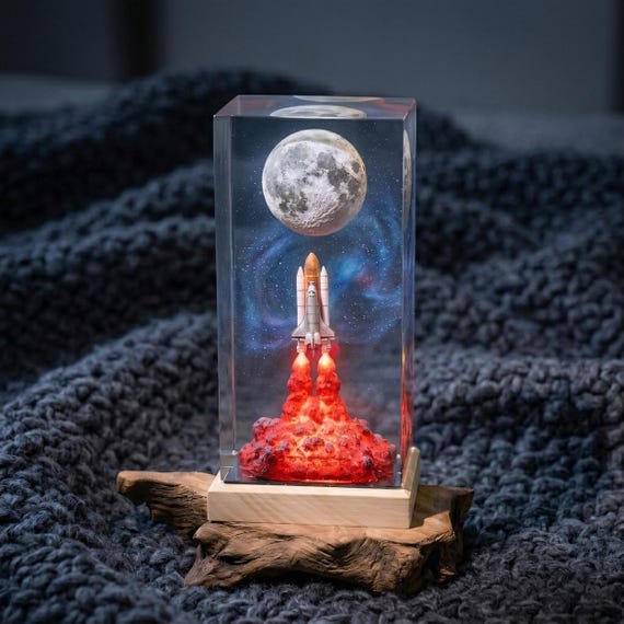 A resin-encased rocket launch scene frozen mid-blast — looks like a tiny NASA mission captured in amber, and it glows.