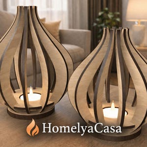 May include: Two wooden candle holders with a teardrop design. Each holder has a circular base and vertical wooden slats. A lit candle sits inside each holder. The logo "HomelyaCasa" is at the bottom.