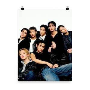 Può includere: Un poster con un gruppo di sette persone con i capelli scuri, in posa su uno sfondo bianco. Indossano un mix di abiti neri e denim. L'immagine è tenuta ferma da due clip argentate.