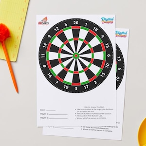 Puede incluir: Dos impresiones de dianas con círculos concéntricos negros, verdes y rojos, numerados del 1 al 20. Las impresiones tienen el texto "Hot Shots" y "Digital Designs". También se ve un bloc de notas amarillo con un bolígrafo naranja y una taza amarilla con un líquido marrón.