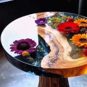 May include: A round side table with a clear resin top inlaid with colorful flowers and a wooden base. The flowers include purple, red, and yellow blooms. The table has a natural wood grain pattern.