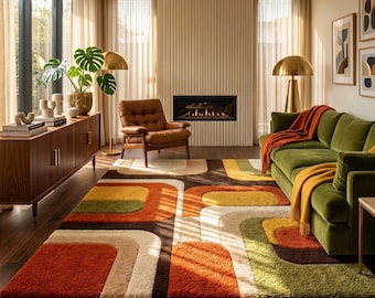 May include: A rectangular area rug featuring a geometric pattern of rounded shapes in shades of orange, yellow, olive green, brown, and cream. The rug is placed on a dark wood floor in a living room with a green velvet sofa and a brown leather chair.