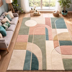 May include: A large, rectangular area rug with a geometric design. The rug features a pattern of squares, rectangles, and arches in shades of pink, green, beige, and blue. The rug is placed on a hardwood floor.